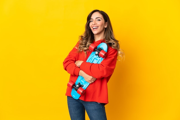 Jeune femme de race blanche isolée sur un mur jaune avec un patin avec une expression heureuse