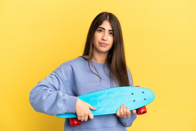 Jeune femme de race blanche isolée sur un mur jaune avec un patin