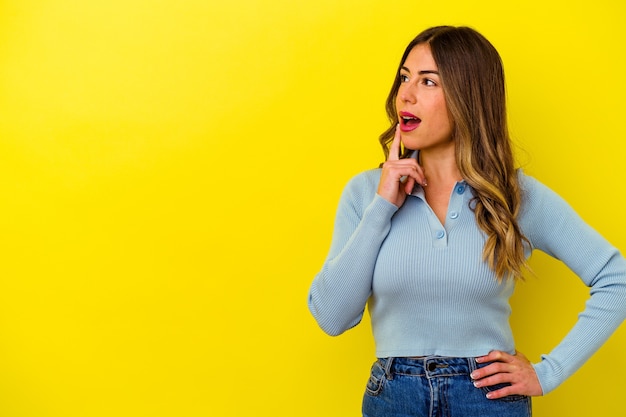 Jeune femme de race blanche isolée sur un mur jaune à la recherche de côté avec une expression douteuse et sceptique.