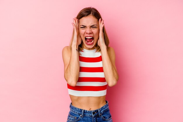 Jeune femme de race blanche isolée sur un mur rose couvrant les oreilles avec les mains en essayant de ne pas entendre un son trop fort