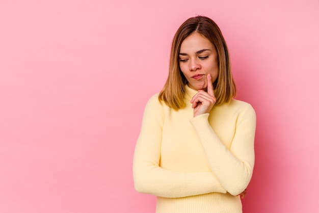 Jeune femme de race blanche isolée sur un mur rose à la recherche de côté avec une expression douteuse et sceptique