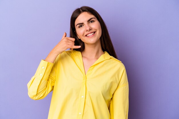 Jeune femme de race blanche isolée sur un mur violet montrant un geste d'appel de téléphone mobile avec les doigts