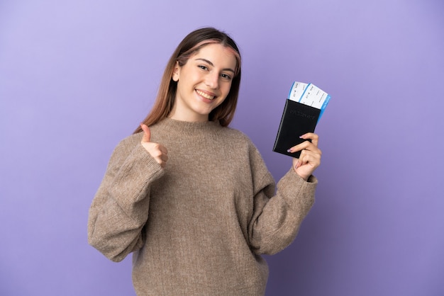 Jeune femme de race blanche isolée sur un mur violet en vacances tenant un passeport et un avion avec le pouce vers le haut