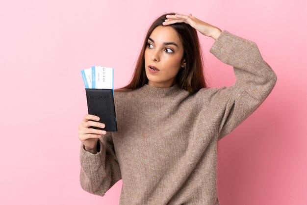 Jeune femme de race blanche isolée sur rose en vacances avec passeport et billets d'avion tout en regardant quelque chose au loin