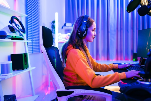 Une jeune femme de race blanche joueuse professionnelle portant un sweat à capuche jaune est assise sur une chaise avec une table de jeu avec un microphone de moniteur de clavier d'ordinateur Préparez-vous pour le jeu de la compétition ou enregistrez un podcast