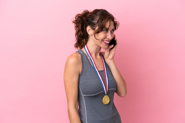 Jeune femme de race blanche avec des médailles isolées sur fond rose gardant une conversation avec le téléphone portable avec quelqu'un