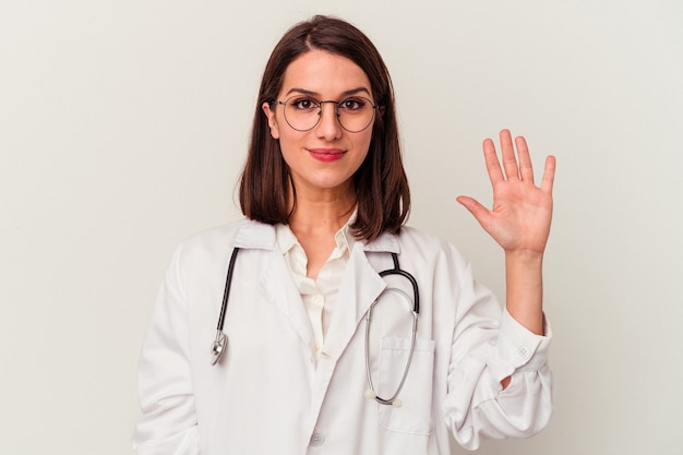 Jeune femme de race blanche médecin isolée sur fond blanc souriant joyeux montrant le numéro cinq avec les doigts.