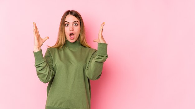 Jeune femme de race blanche sur un mur rose célébrant une victoire