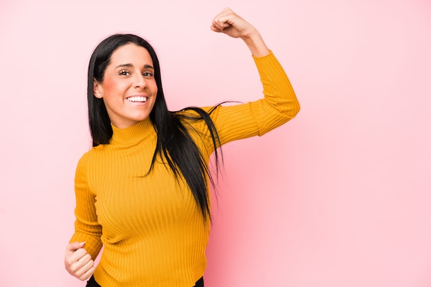 Jeune femme de race blanche sur un mur rose levant le poing après une victoire