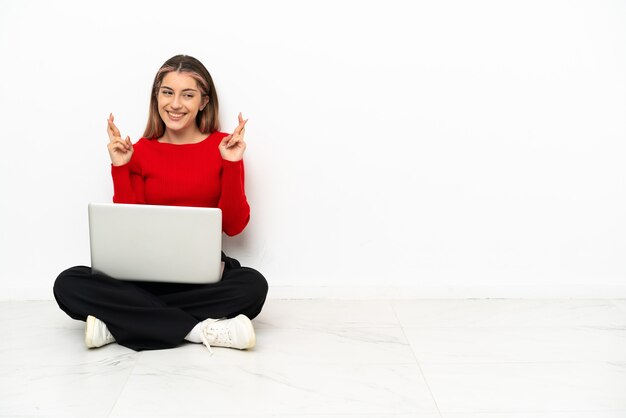 Jeune femme de race blanche avec un ordinateur portable assis sur le sol avec les doigts qui se croisent