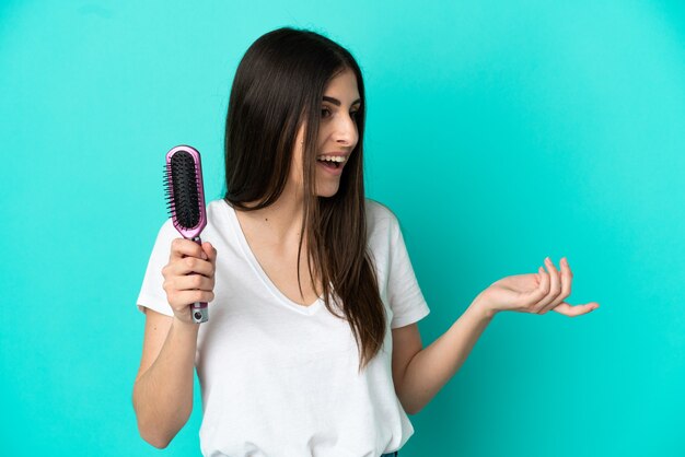 Jeune femme de race blanche avec un peigne à cheveux isolé sur fond bleu avec une expression faciale surprise