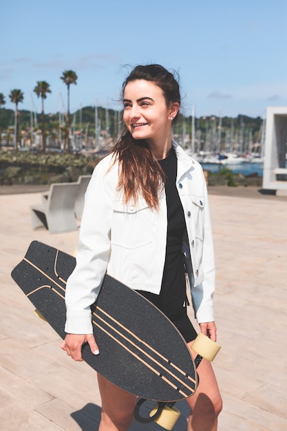 Jeune femme de race blanche portant un longboard au bord de la mer