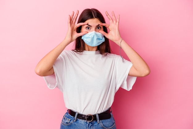 Jeune femme de race blanche portant un masque pour virus isolé sur mur rose en gardant les yeux ouverts pour trouver une opportunité de succès