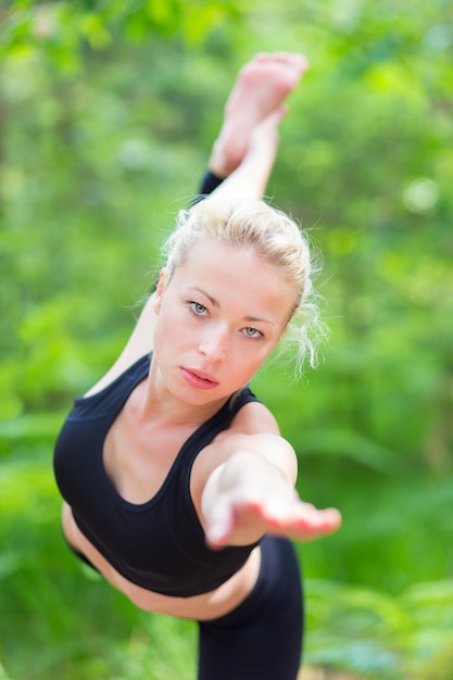 Une jeune femme de race blanche pratique la pose de yoga bikram dans la nature.