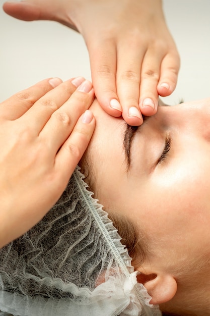 Jeune femme de race blanche recevant un massage du visage par les mains de l'esthéticienne dans un salon médical spa