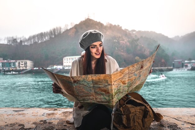 Jeune femme de race blanche regardant une carte lors d'une visite d'une ville au bord de la mer.