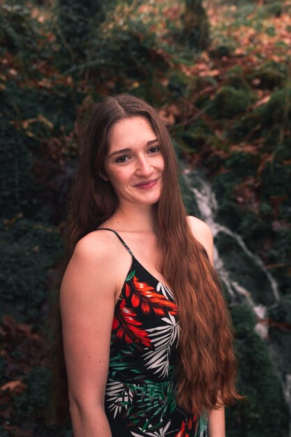 Jeune femme de race blanche avec une robe colorée au milieu de la forêt à côté d'une petite rivière