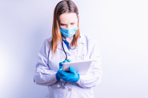 Jeune femme de race blanche avec une robe de masque et un stéthoscope regardant des rapports médicaux sur un concept de tablette de point de médecine et de connectivité technologique