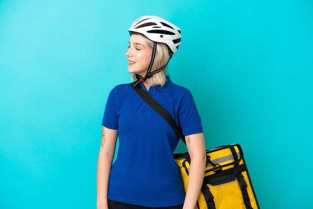 Jeune femme de race blanche avec sac à dos thermique isolé sur fond bleu regardant sur le côté