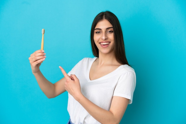 Jeune femme de race blanche se brosser les dents isolées sur fond bleu et le pointant