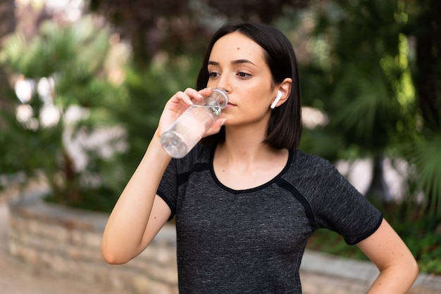 Jeune femme de race blanche sport avec une bouteille d'eau à l'extérieur dans un parc