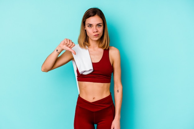 Jeune femme de race blanche sport isolée sur fond bleu montrant un geste de dégoût, les pouces vers le bas. Concept de désaccord.