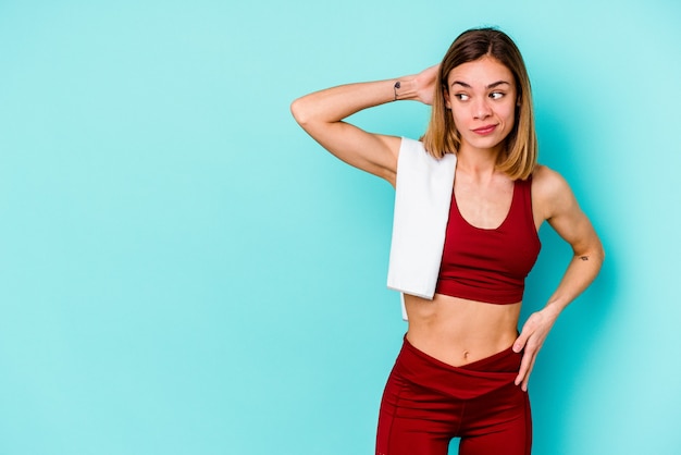 Jeune femme de race blanche sport isolée sur fond bleu, toucher l'arrière de la tête, penser et faire un choix.