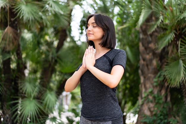 Jeune femme de race blanche sport en position zen à l'extérieur dans un parc