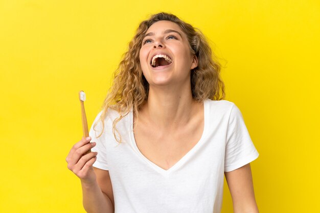 Jeune femme de race blanche tenant un brossage des dents isolé sur fond jaune en riant