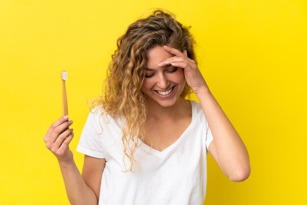 Jeune femme de race blanche tenant un brossage des dents isolé sur fond jaune en riant