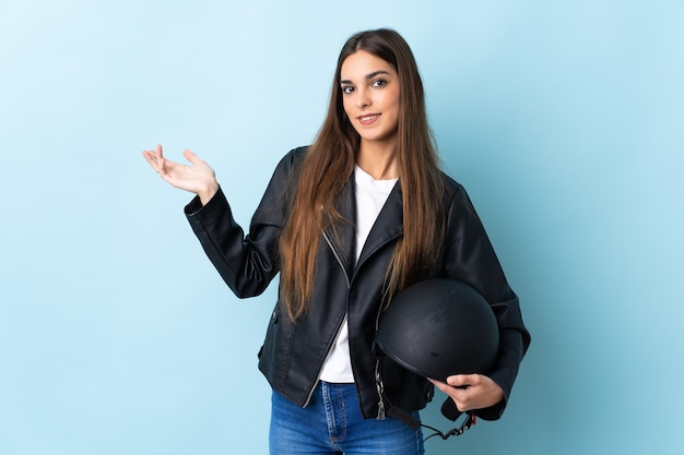 Jeune femme de race blanche tenant un casque de moto sur le bleu étendant les mains sur le côté pour inviter à venir