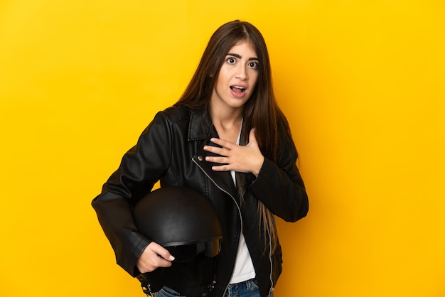 Jeune femme de race blanche tenant un casque de moto isolé sur fond jaune surpris et choqué tout en regardant à droite