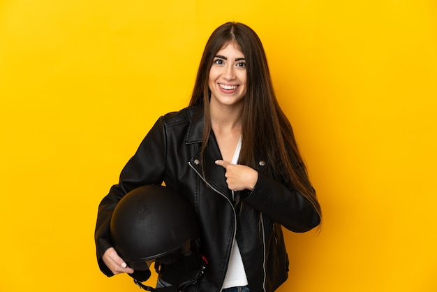 Jeune femme de race blanche tenant un casque de moto isolé sur un mur jaune avec une expression faciale surprise