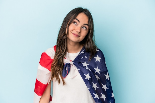 Jeune femme de race blanche tenant un drapeau américain isolé sur fond bleu rêvant d'atteindre des objectifs et des objectifs