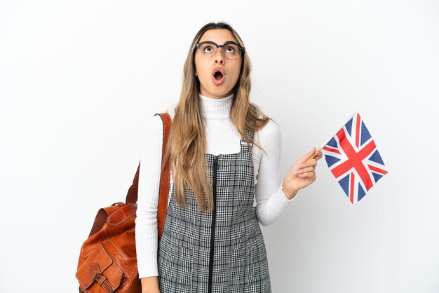 Jeune femme de race blanche tenant un drapeau du Royaume-Uni isolé sur fond blanc en levant et avec une expression surprise