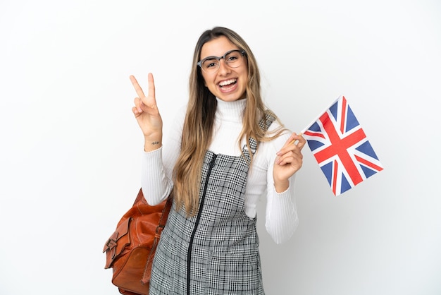 Jeune femme de race blanche tenant un drapeau du Royaume-Uni isolé sur fond blanc souriant et montrant le signe de la victoire