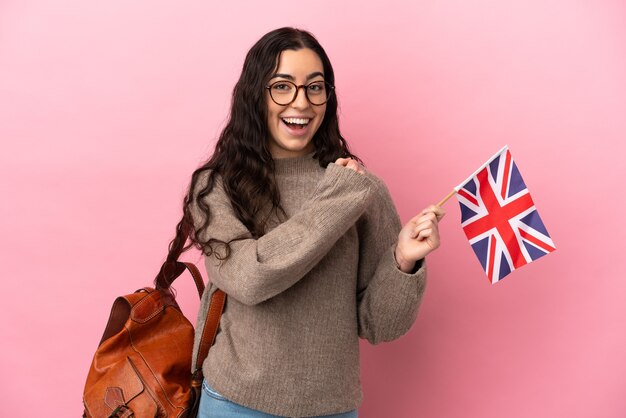 Jeune femme de race blanche tenant un drapeau du Royaume-Uni isolé sur fond rose célébrant une victoire