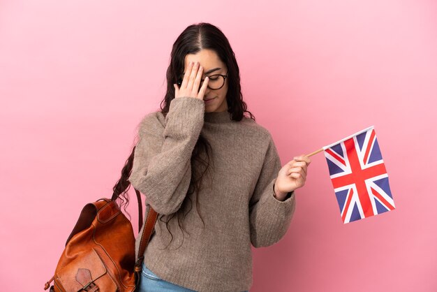 Jeune femme de race blanche tenant un drapeau du Royaume-Uni isolé sur fond rose avec une expression fatiguée et malade