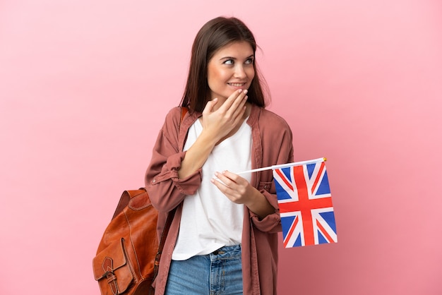 Jeune femme de race blanche tenant un drapeau du Royaume-Uni isolé sur fond rose en levant tout en souriant