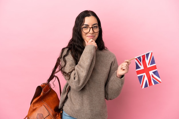 Jeune femme de race blanche tenant un drapeau du Royaume-Uni isolé sur un mur rose et levant