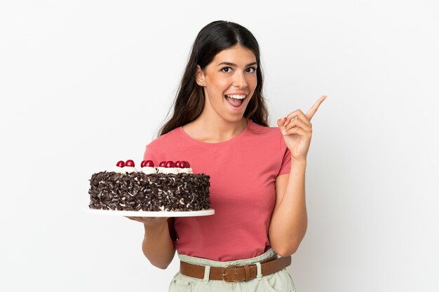 Jeune femme de race blanche tenant un gâteau d'anniversaire isolé sur fond blanc en pensant à une idée pointant le doigt vers le haut