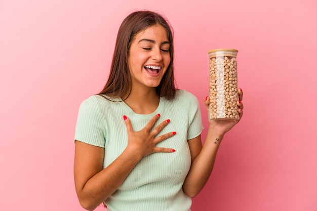 Jeune femme de race blanche tenant un pot de pois chiches isolé sur fond rose éclate de rire en gardant la main sur la poitrine.