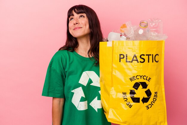 Jeune femme de race blanche tenant un sac en plastique recyclé isolé sur fond rose rêvant d'atteindre les objectifs et les fins