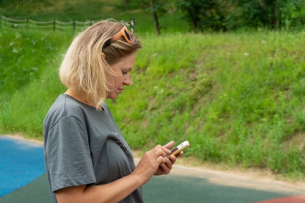Une jeune femme de race blanche en tenue de sport se tient dans la rue avec un téléphone dans les mains.