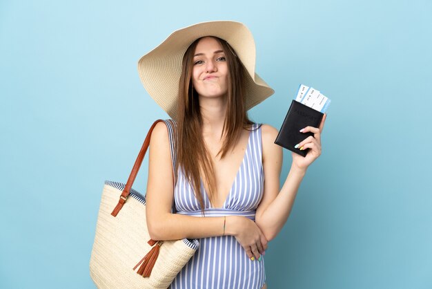 Jeune femme de race blanche en vacances d'été tenant un passeport isolé sur fond bleu avec une expression triste