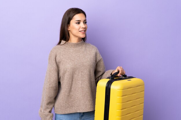 Jeune femme de race blanche sur violet en vacances avec valise de voyage