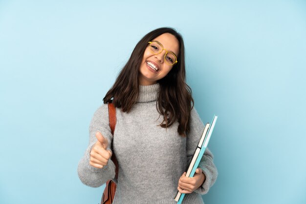 Jeune femme de race mixte allant à l'école sur le mur bleu avec les pouces vers le haut parce que quelque chose de bien s'est produit