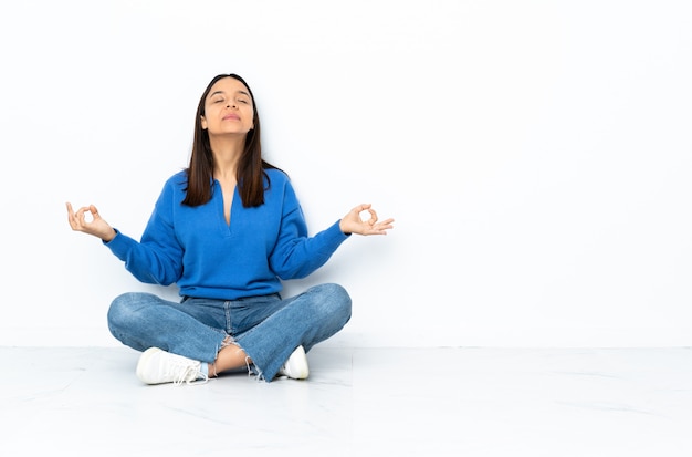 Jeune femme de race mixte assis sur le sol isolé sur blanc dans une pose zen