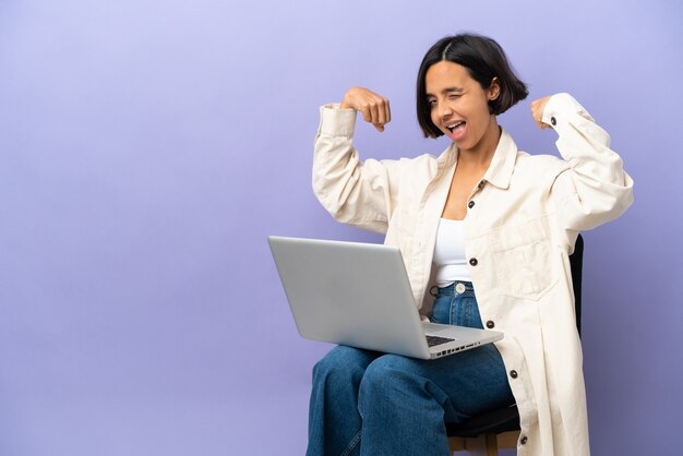 Jeune femme de race mixte assise sur une chaise avec un ordinateur portable isolé sur fond violet faisant un geste fort