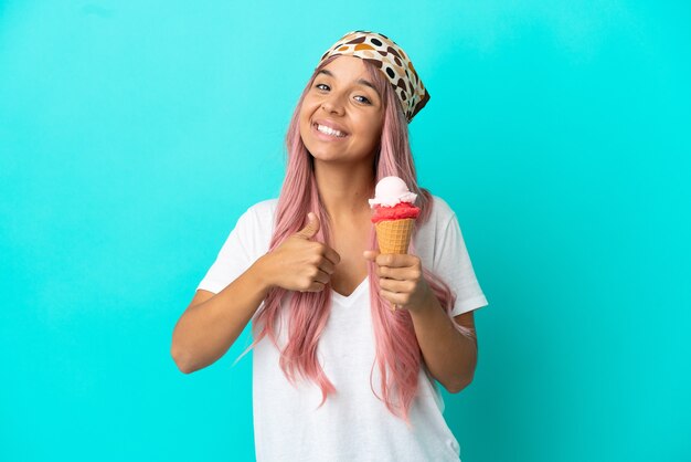 Jeune femme de race mixte avec une glace au cornet isolée sur fond bleu donnant un geste du pouce vers le haut